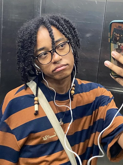 A young man with glasses and a striped shirt is taking a selfie.