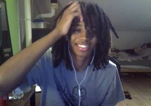 A young man with dreadlocks smiles at the camera.