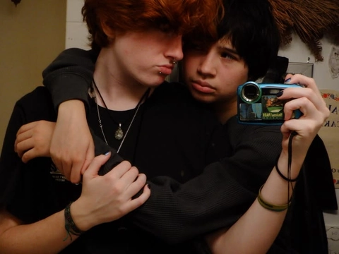 A couple of young men holding up a cell phone.