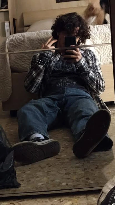 A man sitting on the floor taking a picture of himself in a mirror.