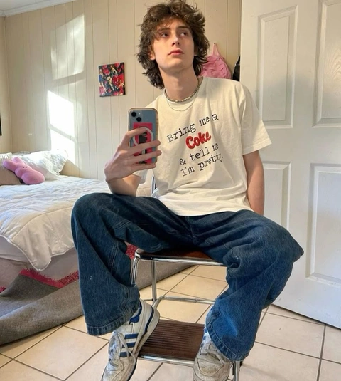 A young man sitting on a stool taking a selfie.
