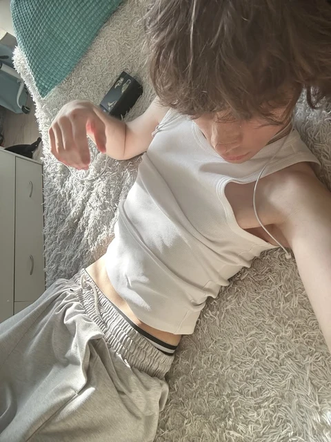 A woman in a white shirt and gray pants laying on a bed.