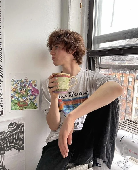 A man holding a cup of coffee in front of a window.