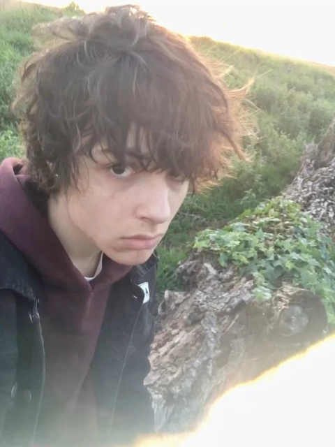 A young man with curly hair standing next to a tree.
