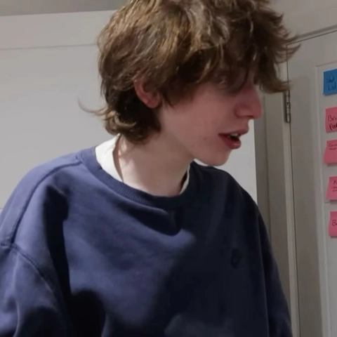 A young man with curly hair standing in front of a door.