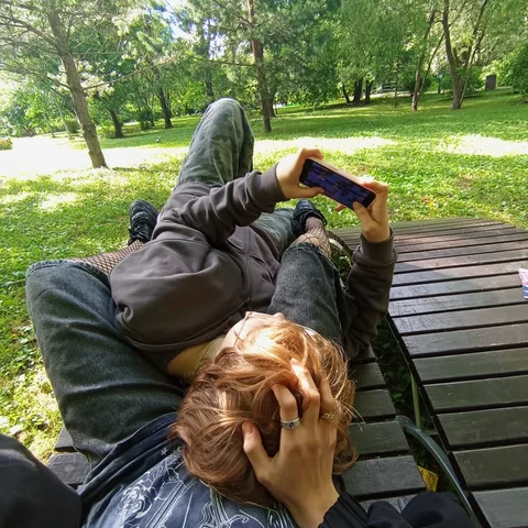 A couple of people laying on top of a wooden bench.