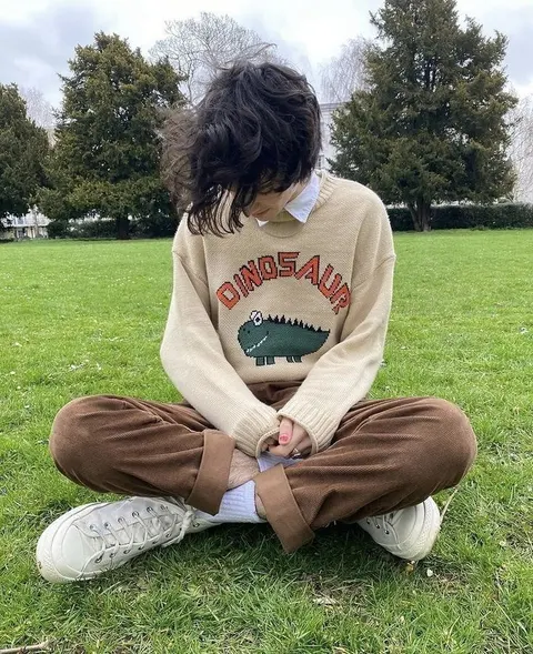 A man sitting on the grass wearing a sweater that says Dinosau.
