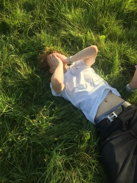 A man laying in the grass with his hands on his head.