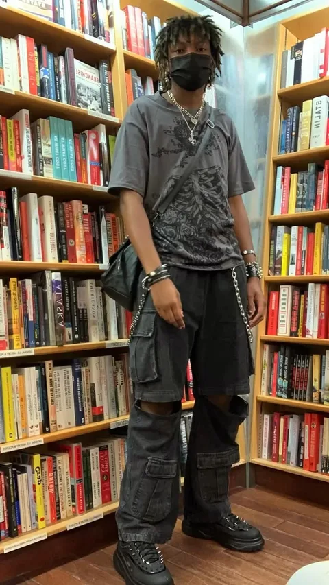 A man wearing a face mask standing in front of a book shelf.