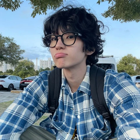 A young boy with curly hair wearing glasses and a plaid shirt.