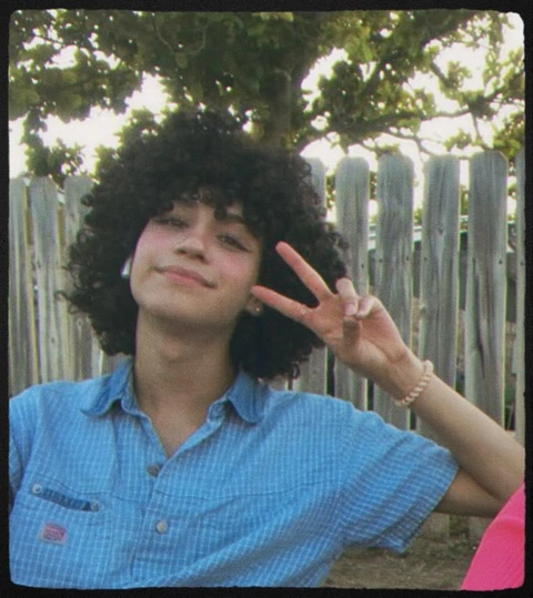 A woman with curly hair making a peace sign.