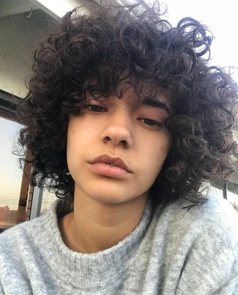 A young boy with curly hair is looking at the camera.