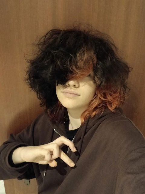 A young man with long curly hair making a peace sign.