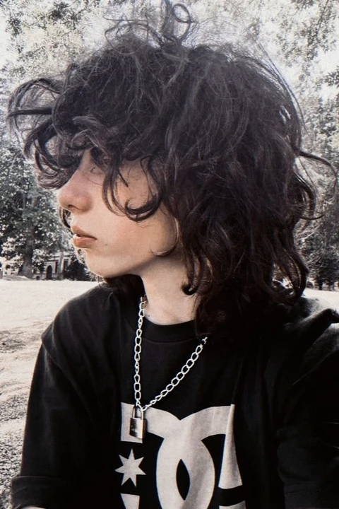 A young man with long curly hair wearing a black shirt.