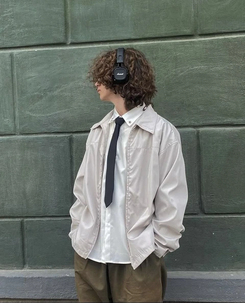 A man with curly hair wearing headphones standing in front of a wall.