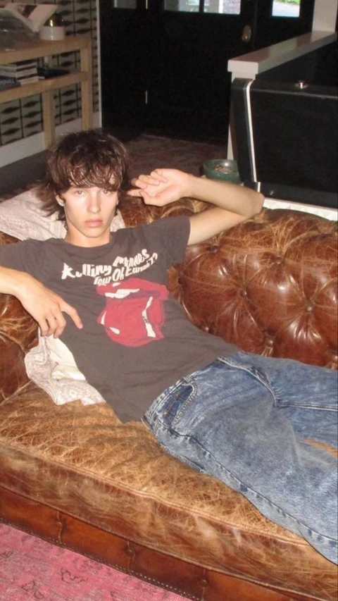 A young man laying on top of a brown couch.
