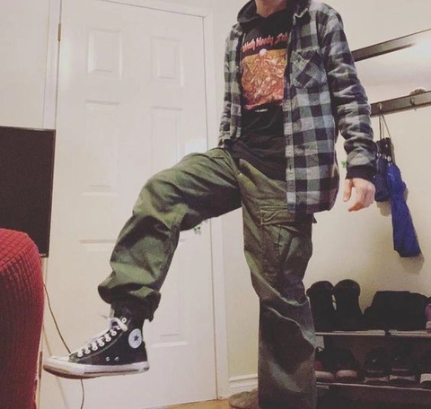 A man in a plaid shirt and green pants standing in front of a door.