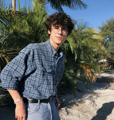 A young man standing in front of a palm tree.
