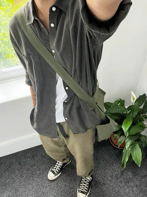 A man in a black shirt and khaki pants holding a green bag.