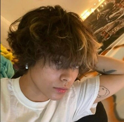A young boy with curly hair and a tattoo on his arm.