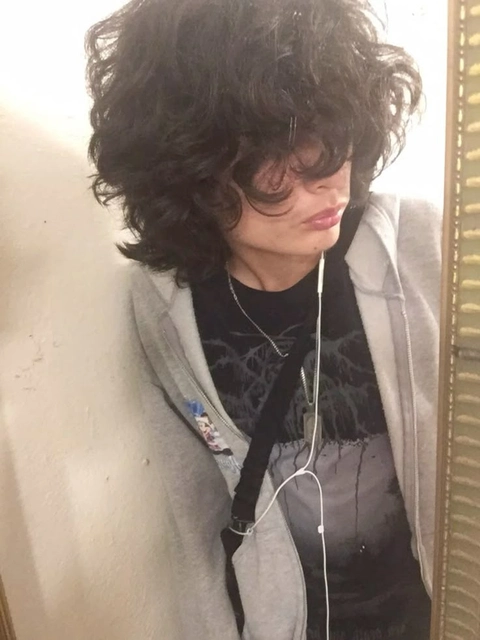A young man with curly hair is reflected in a mirror.