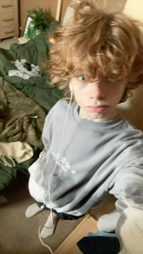 A young boy with curly hair sitting on a bed.