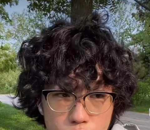A woman with curly hair and glasses in front of a tree.