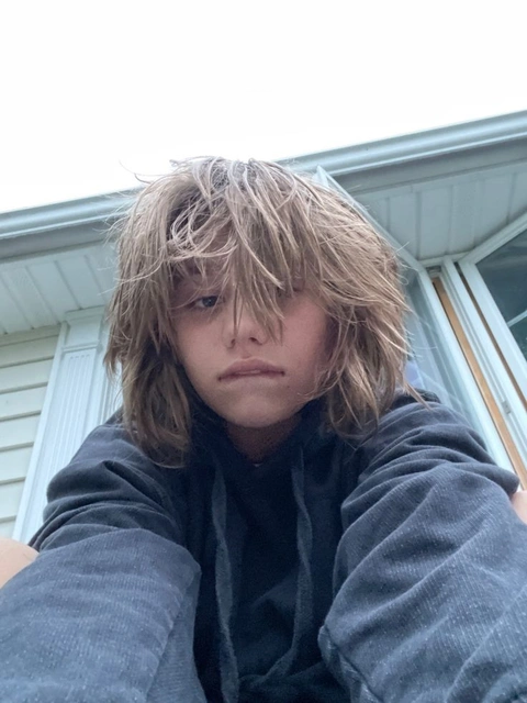 A young man with long hair sitting on the ground.